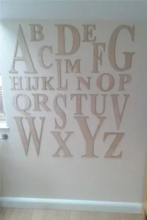 Drewniany alfabet wycięty laserem z naturalnej sklejki, zamocowany na ścianie w pokoju dziecięcym