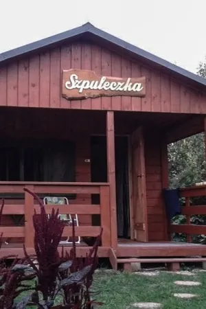 Napis: 'Szpuleczka' wycięty laserem z jasnej sklejki, zamocowany na elewacji drewnianego domu