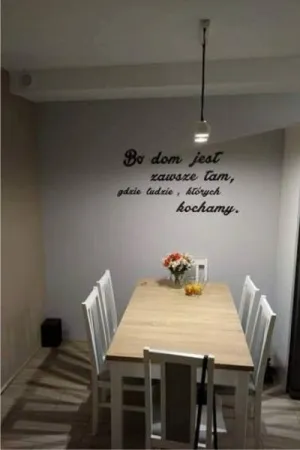 Napis: 'Bo dom jest zawsze tam, gdzie ludzie, których kochamy' wycięty laserem z czarnej sklejki, na ścianie w jadalni