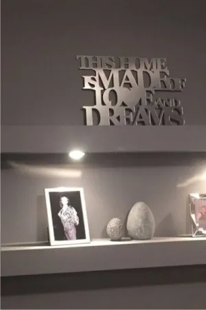 Napis: 'This home is made of love and dreams' wycięty laserem z lustrzanej plexi, zamocowany na ciemnej ścianie