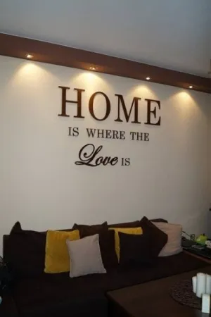 Napis Home is where the love is wykonany ze sklejki, umieszczony na ścianie nad sofą