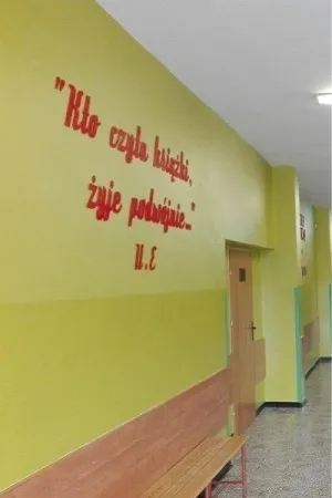 Napis Kto czyta książki, żyje podwójnie wykonany ze sklejki, umieszczony na ścianie szkolnego korytarza