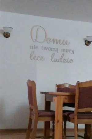 Napis: 'Domu nie tworzą mury, lecz ludzie' wycięty laserem z naturalnej sklejki, umieszczony na ścianie w jadalni
