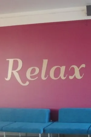 Napis: 'Relax' wycięty laserem z jasnej sklejki, zamocowany na fioletowej ścianie