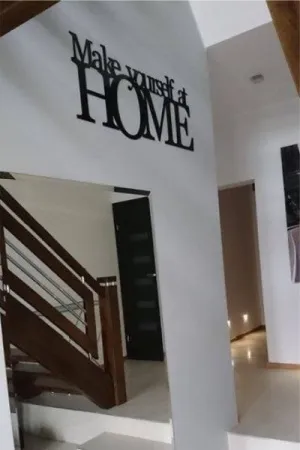 Napis: 'Make yourself at HOME' wycięty laserem z czarnej sklejki, zamocowany na ścianie w holu