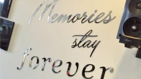 Dekoracyjny napis na ścianie wykonany z lustrzanych liter: Memories stay forever, otoczony elementami audio i zdjęciami.