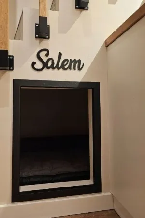 Czarny napis 'Salem' wycięty laserem, zamocowany nad wejściem do małego domku pod schodami
