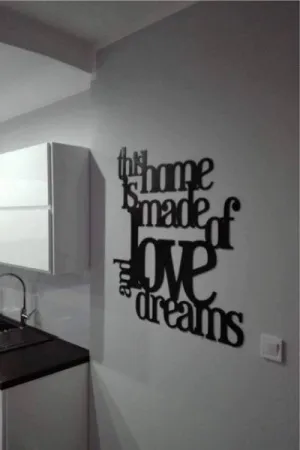 Napis: 'This home is made of love and dreams' wycięty laserem z czarnej sklejki, zamocowany na ścianie w kuchni
