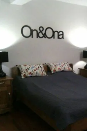 Napis: 'On & Ona' wycięty laserem z czarnej sklejki, zamocowany na ścianie nad łóżkiem w sypialni