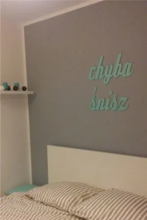 Napis: 'chyba śnisz' wycięty laserem z miętowej sklejki, zamocowany na szarej ścianie w sypialni