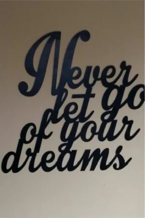 Czarny napis: 'Never let go of your dreams' wycięty laserem na ścianie w minimalistycznym wnętrzu