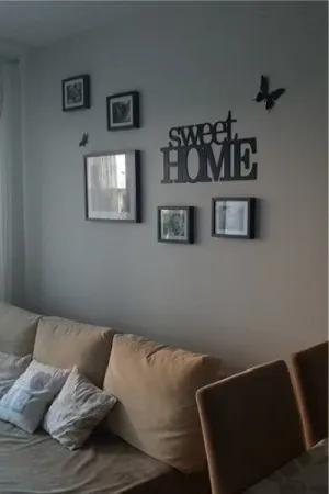 Napis dekoracyjny na ścianie: Sweet Home z ramkami na zdjęcia w przytulnym salonie