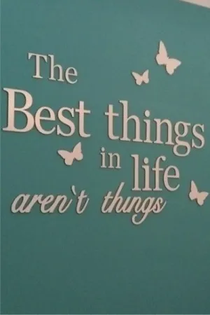 Napis dekoracyjny na ścianie: The best things in life aren't things z motylami na turkusowym tle