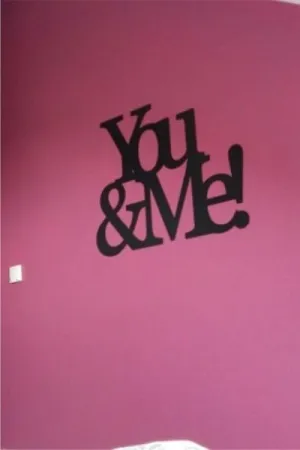 Napis dekoracyjny na ścianie: You & Me w nowoczesnej sypialni z fioletową ścianą