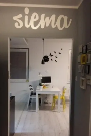Napis: 'siema' wycięty laserem z białej sklejki, umieszczony nad wejściem w nowoczesnym wnętrzu