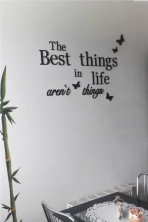 Napis: 'The best things in life aren’t things' z motylkami, wycięty laserem z czarnej sklejki, na jasnej ścianie