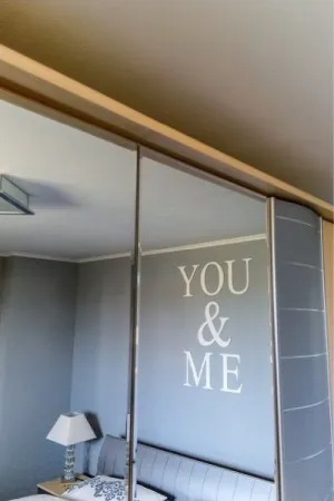 Biały napis: You & Me wycięty laserem, zamocowany na ścianie w eleganckiej sypialni